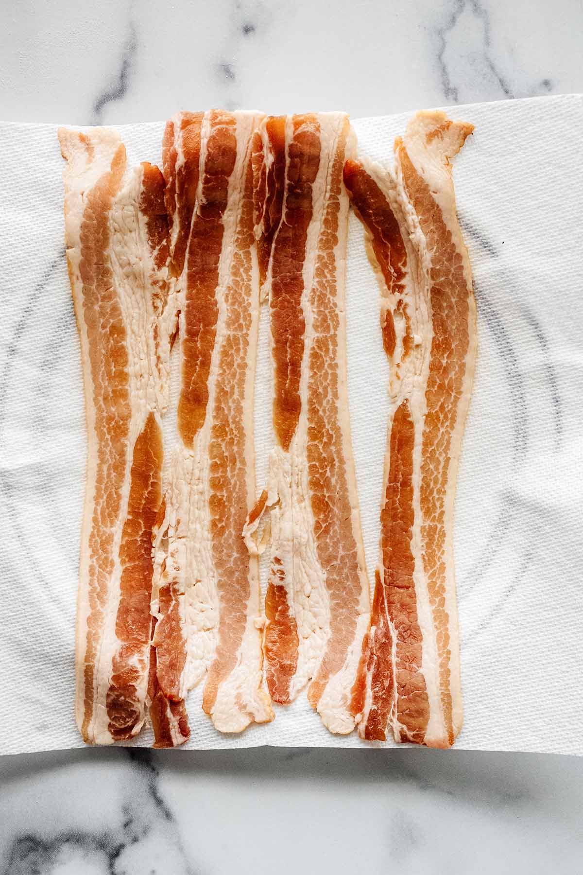 Four strips of bacon on a paper towel on a large plate.