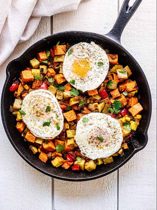 Sweet potato breakfast hash with topped with poached eggs in a cast iron skillet