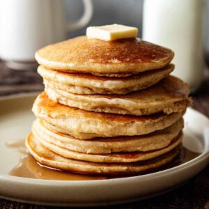 Stack of cassava pancakes on a beige plate with butter and maple syrup.