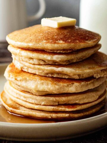 Stack of cassava pancakes on a beige plate with butter and maple syrup.