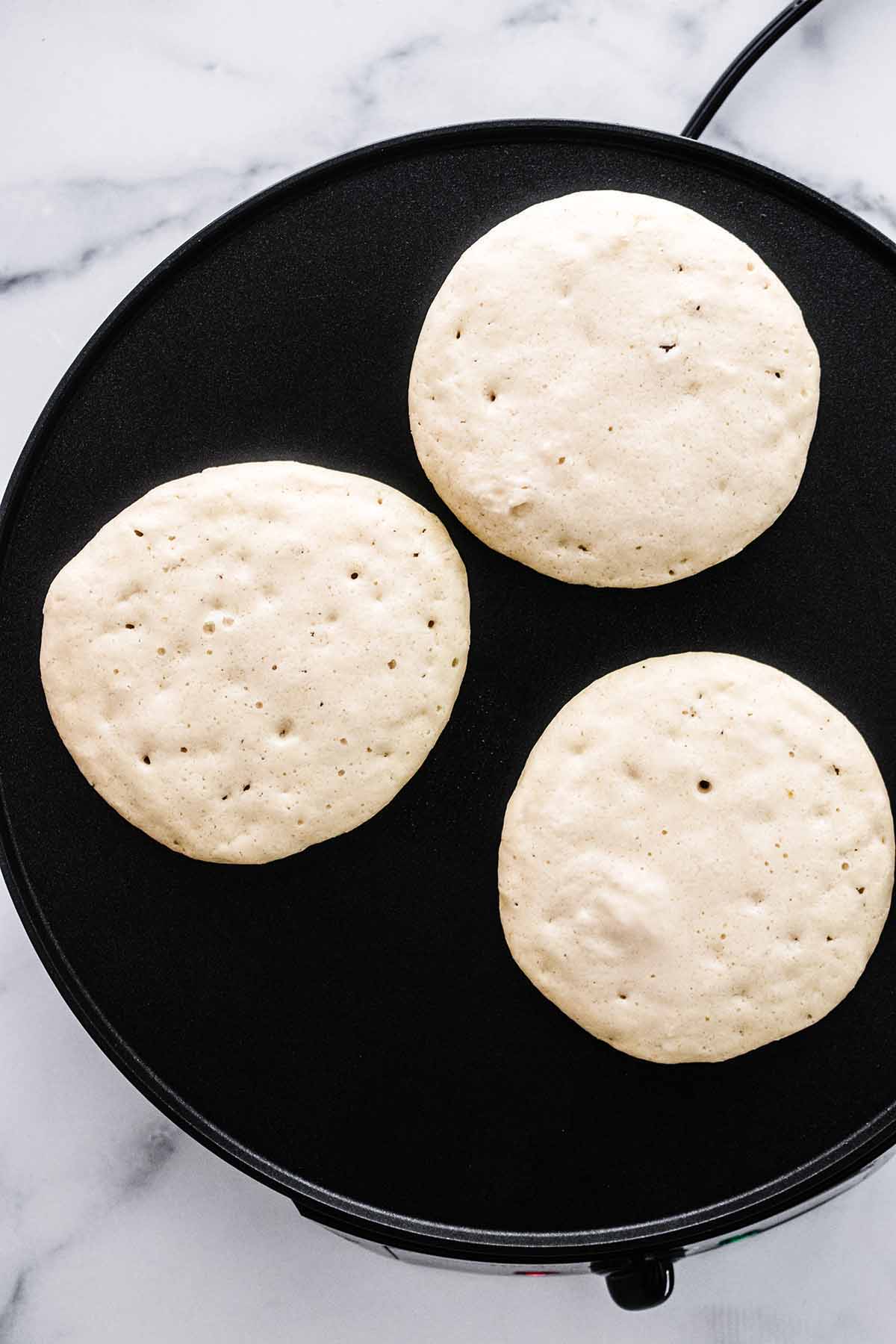 Three cassava flour pancakes bubbling and cooking on a griddle.