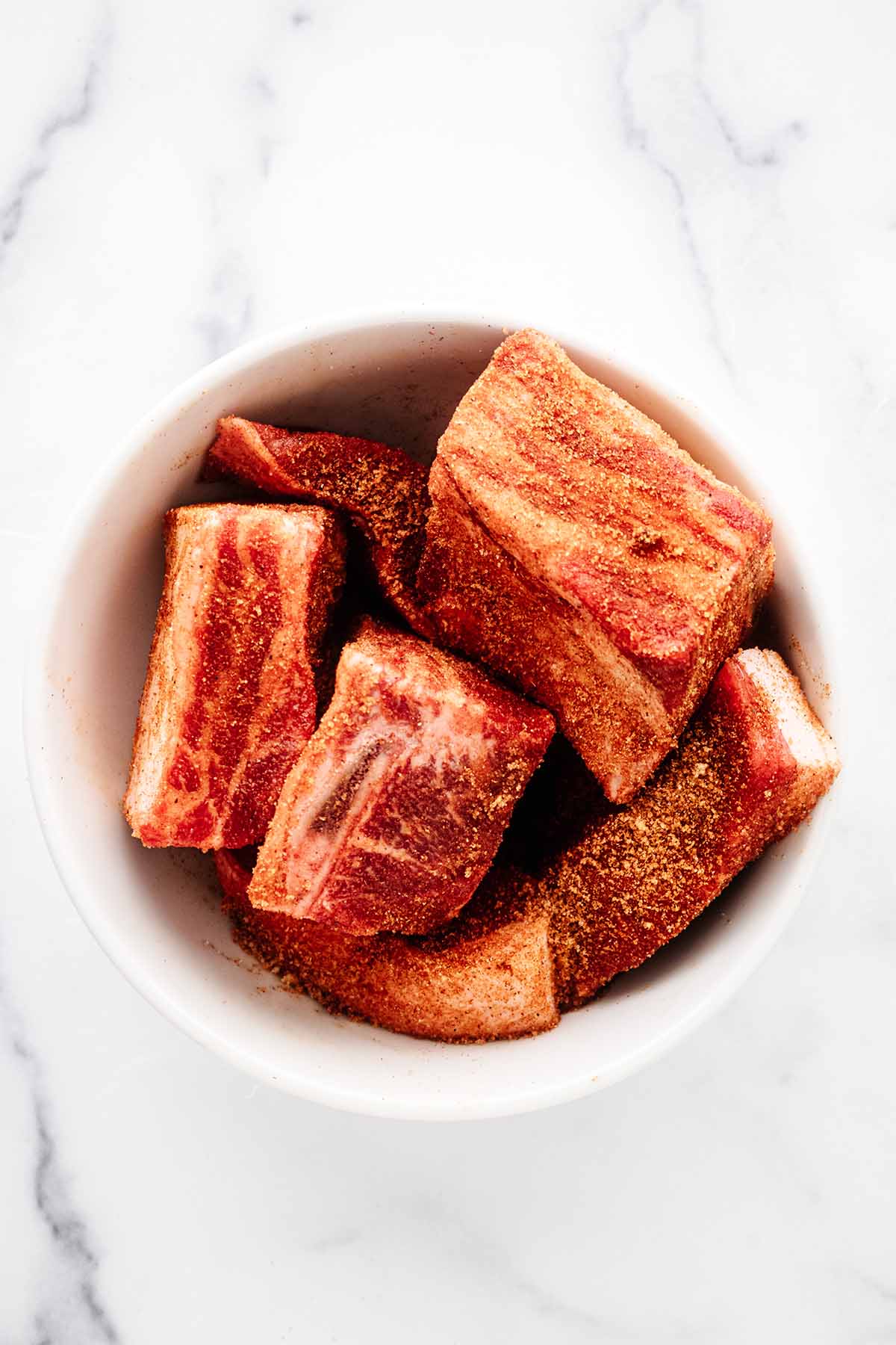 Beef short ribs rubbed with spice rub in a white bowl