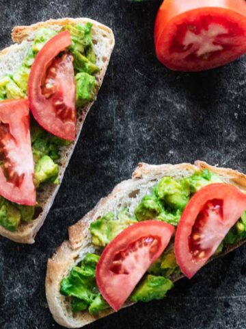 Two slices of avocado tomato toast on a dark marble background.