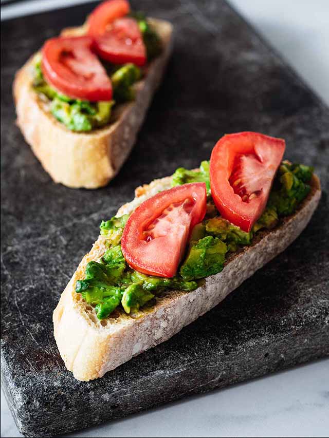 Avocado tomato toast slices on a dark marble cutting board