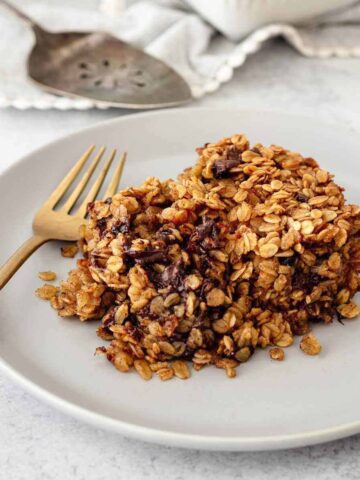 Serving of chocolate chip baked oatmeal on a light grey plate with a gold fork.