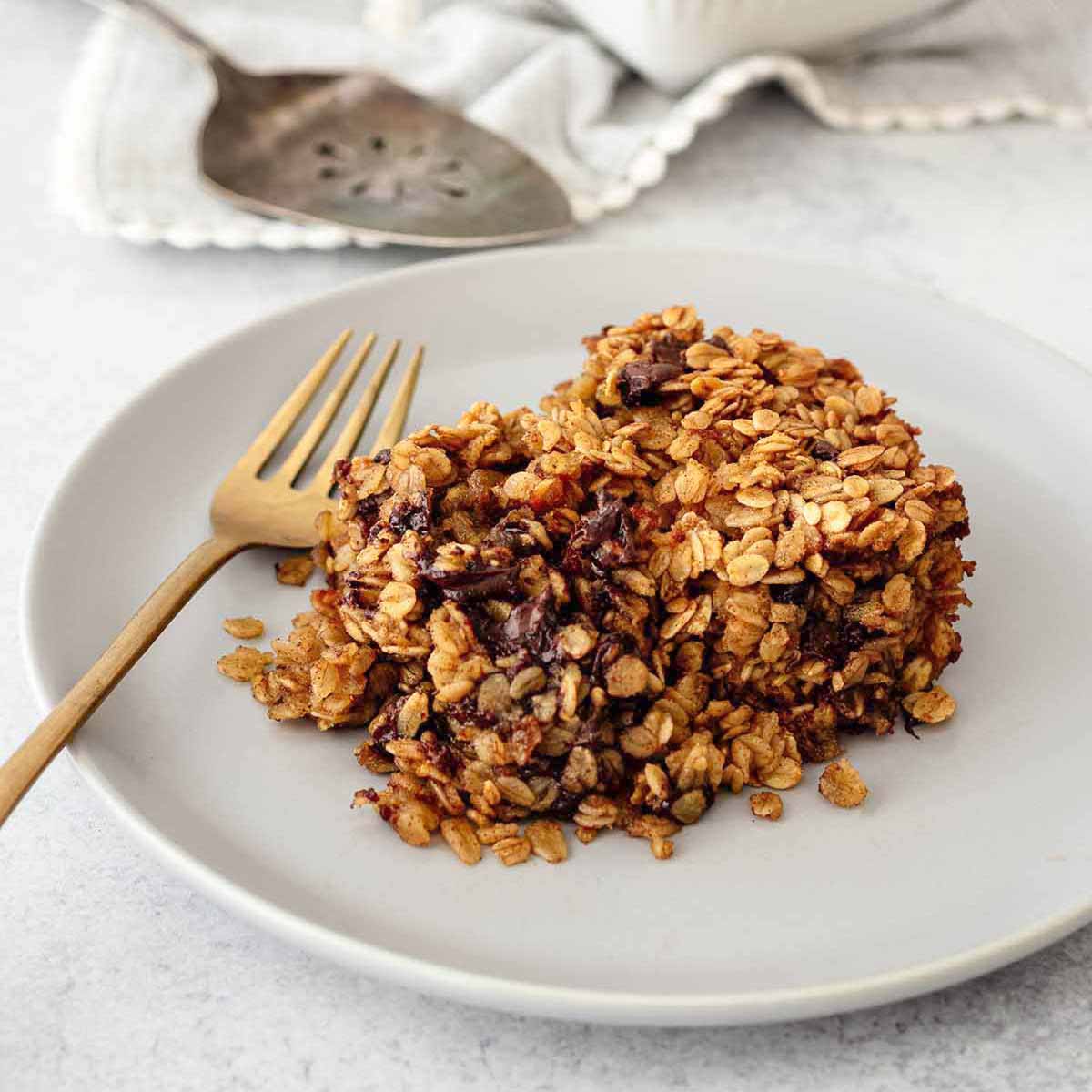 Serving of chocolate chip baked oatmeal on a light grey plate with a gold fork.