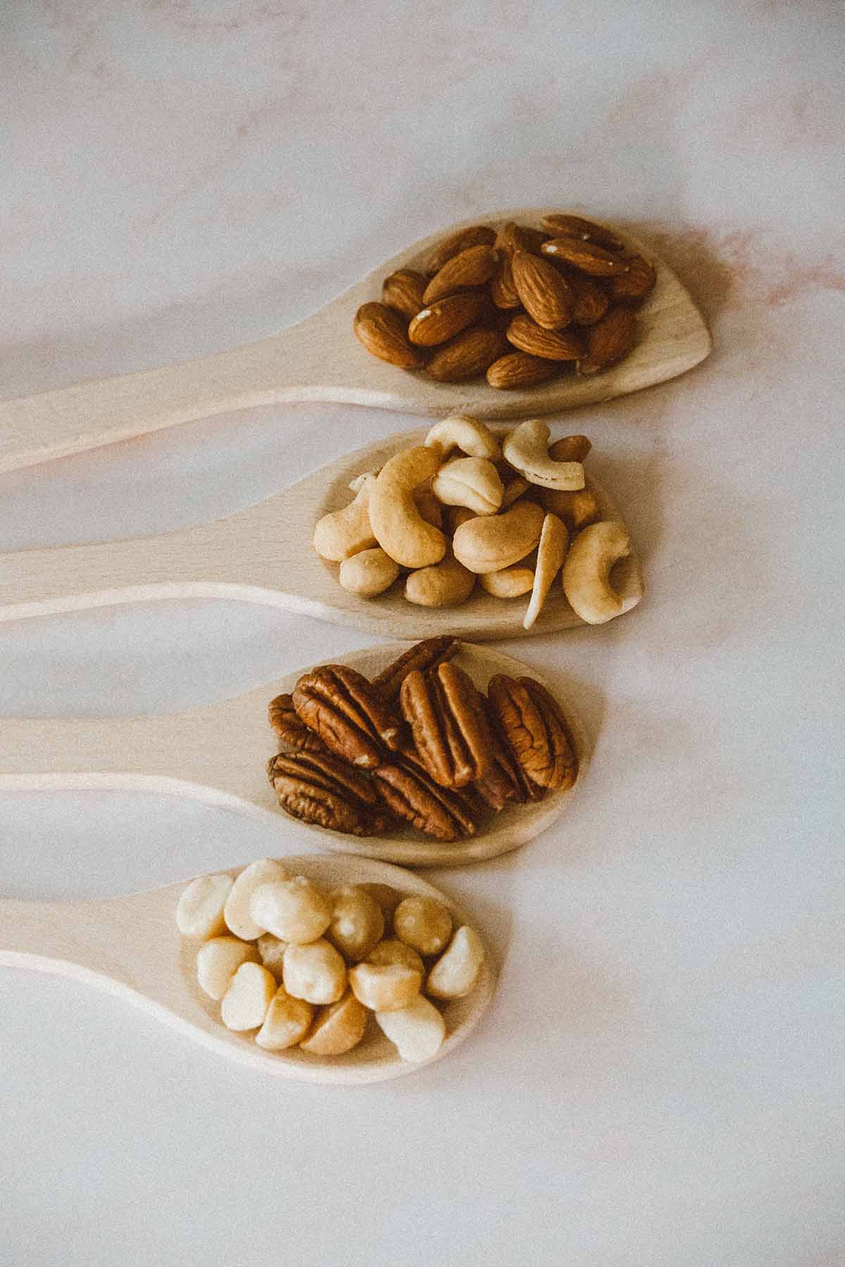 Almonds, cashews, pecans, and macadamia nuts in wooden spoons.