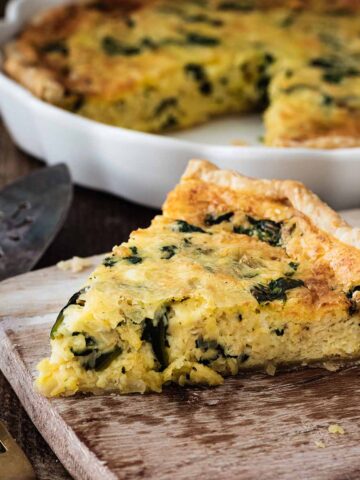 Slice of quiche Florentine on a light wood cutting board.