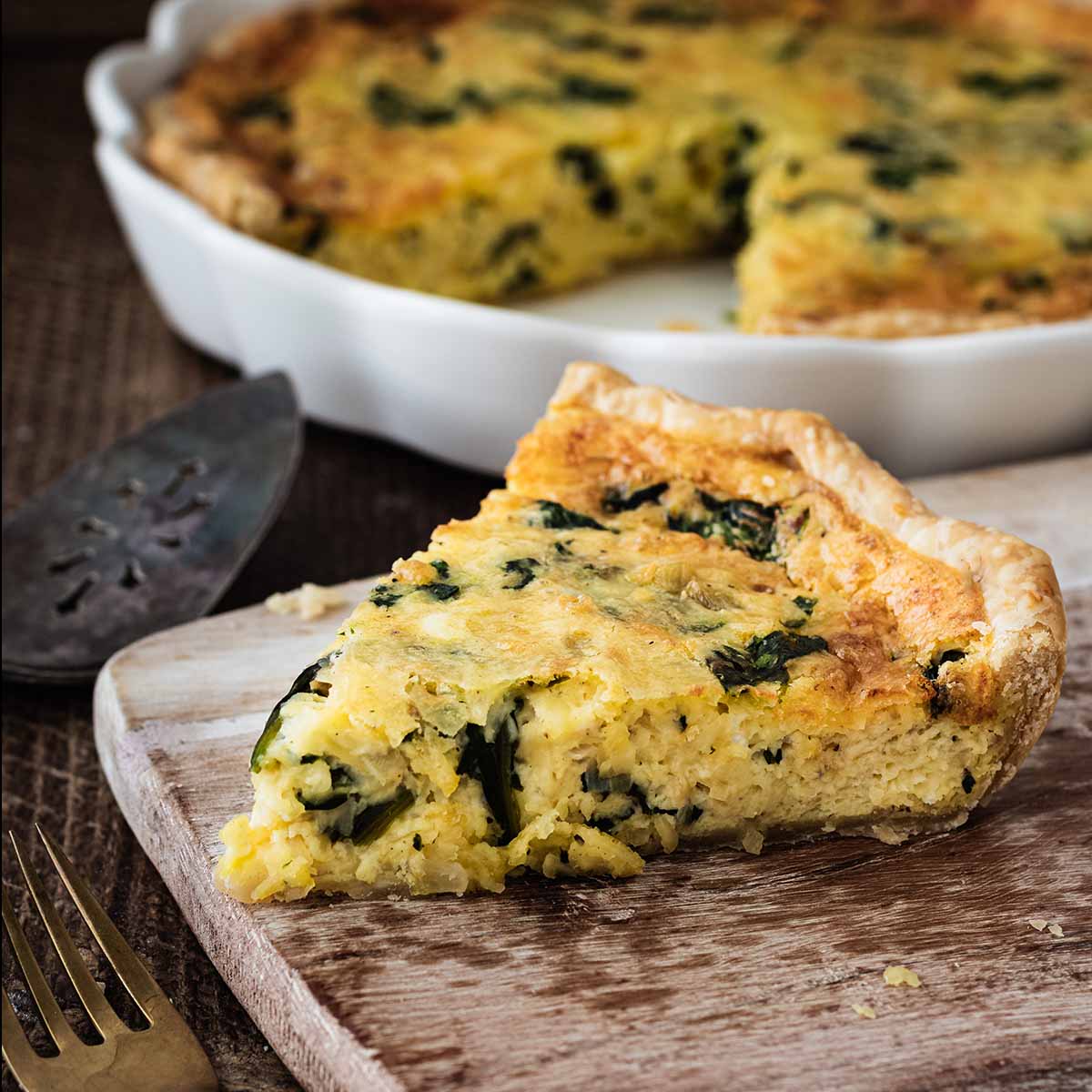 Slice of quiche Florentine on a light wood cutting board.