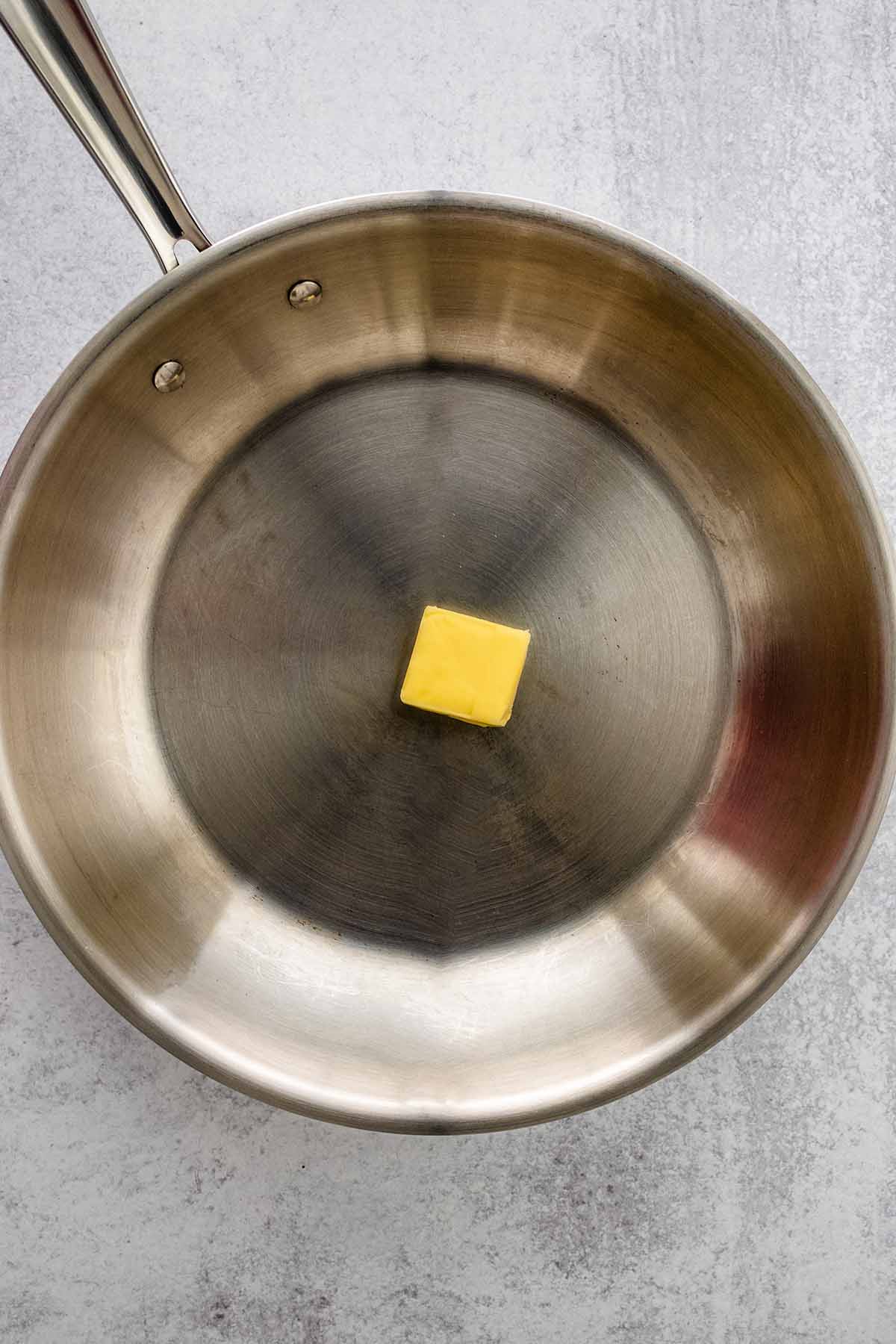 Slab of butter in a stainless steel skillet.