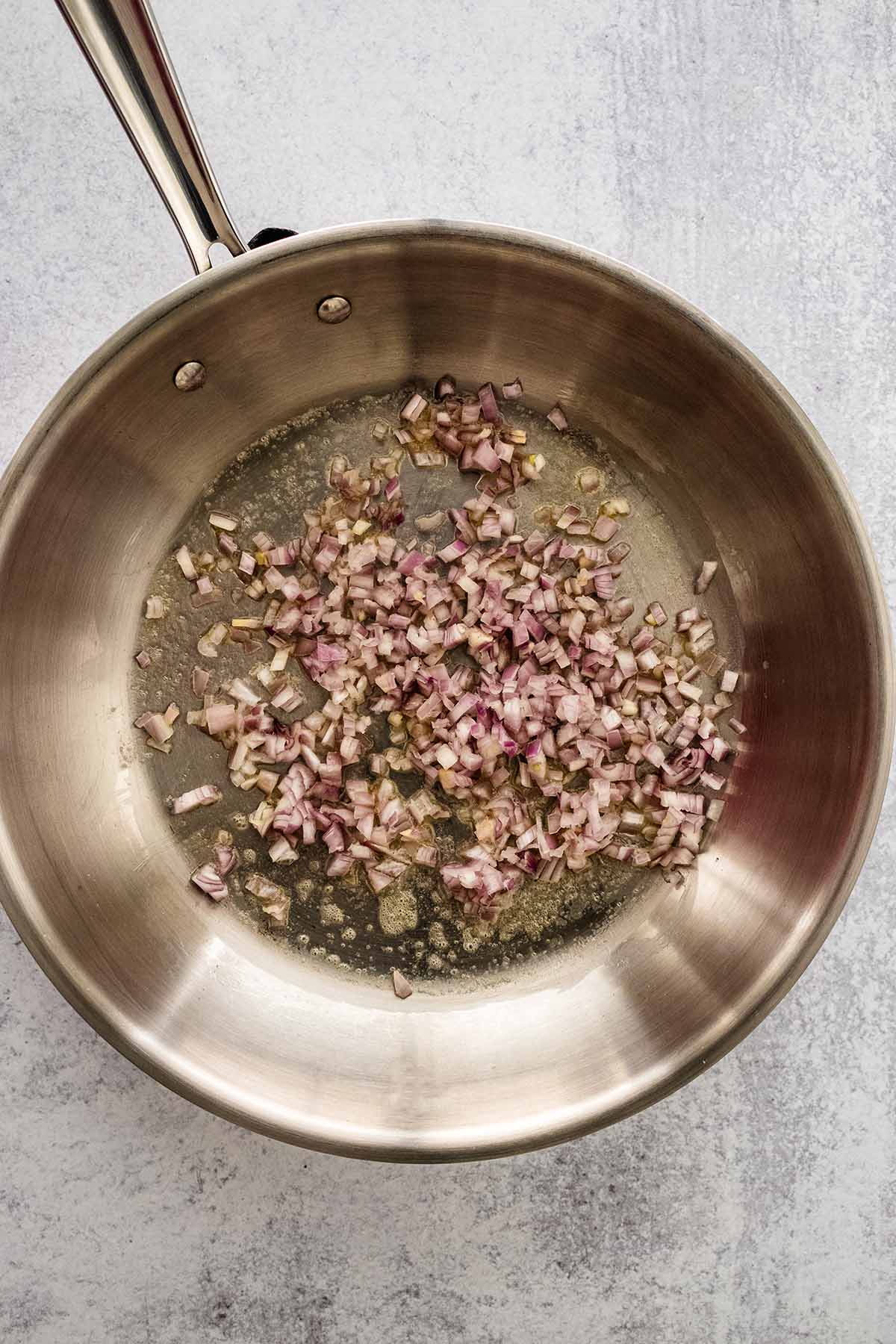 Diced shallot cooking in a stainless steel skillet