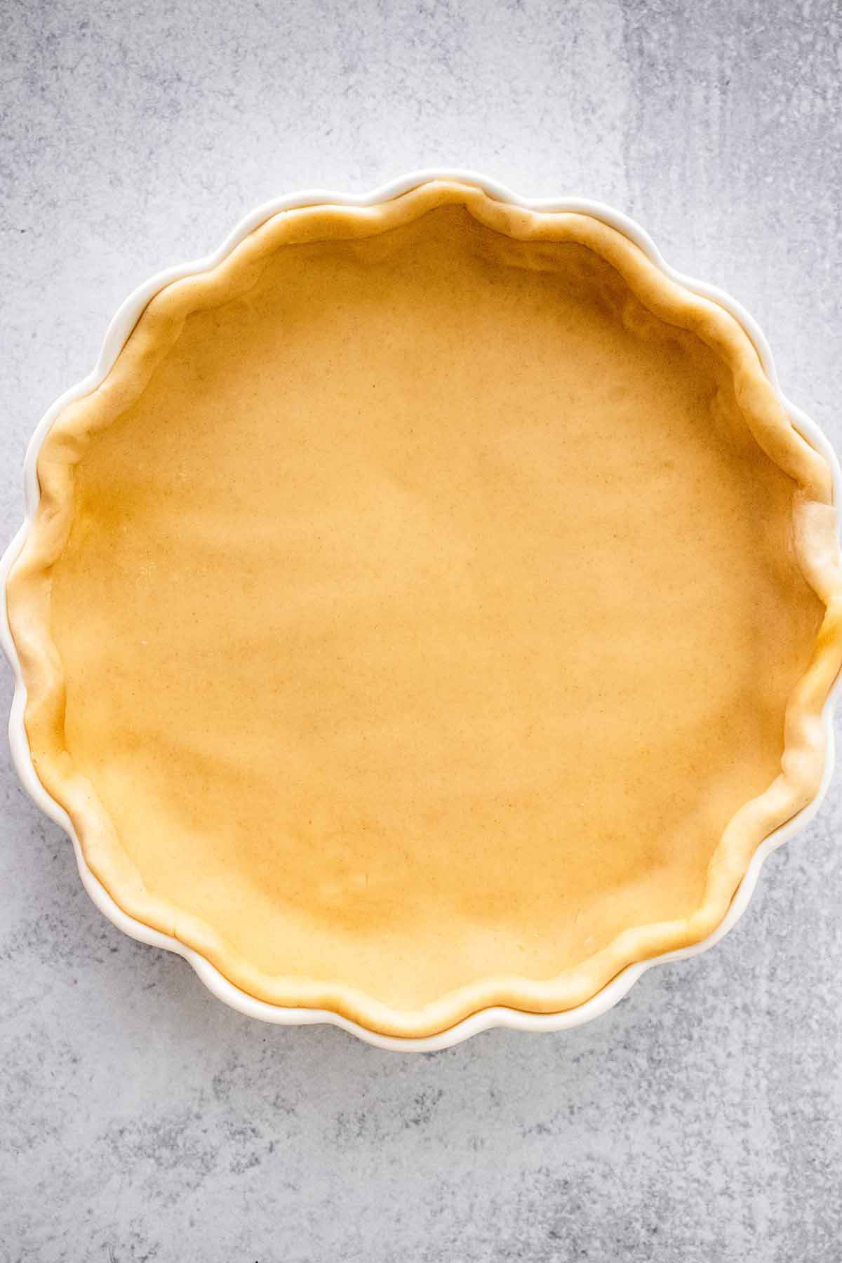 Unbaked pie crust in a white quiche dish.