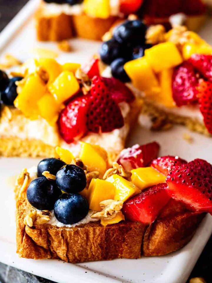 Close up of ricotta toast topped with fresh strawberries, diced mango, and whole blueberries.