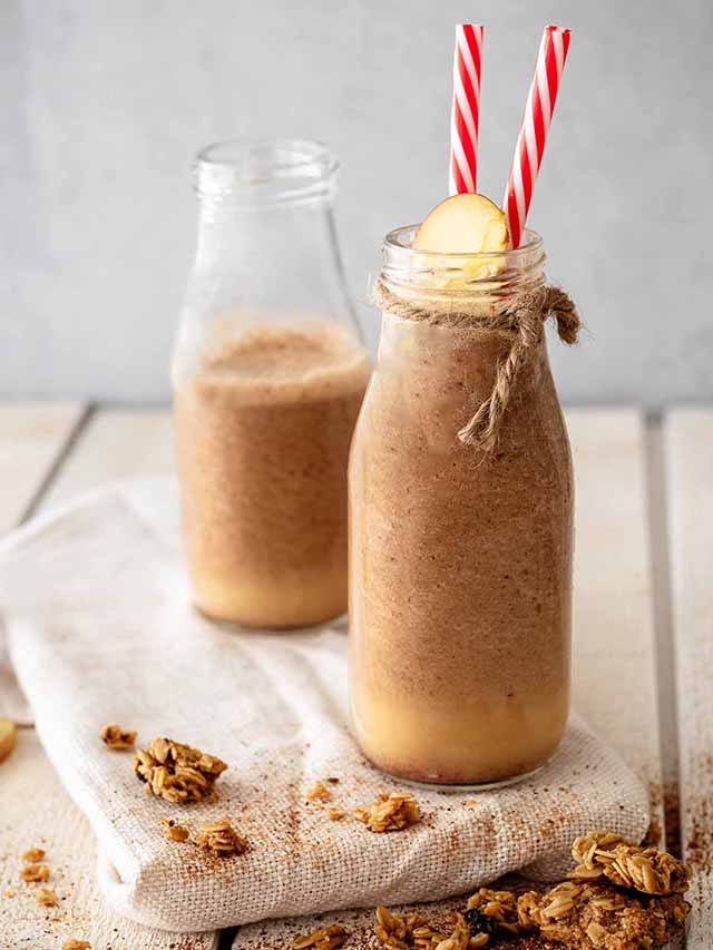 Two apple pie smoothies in milk bottles with red and white straws