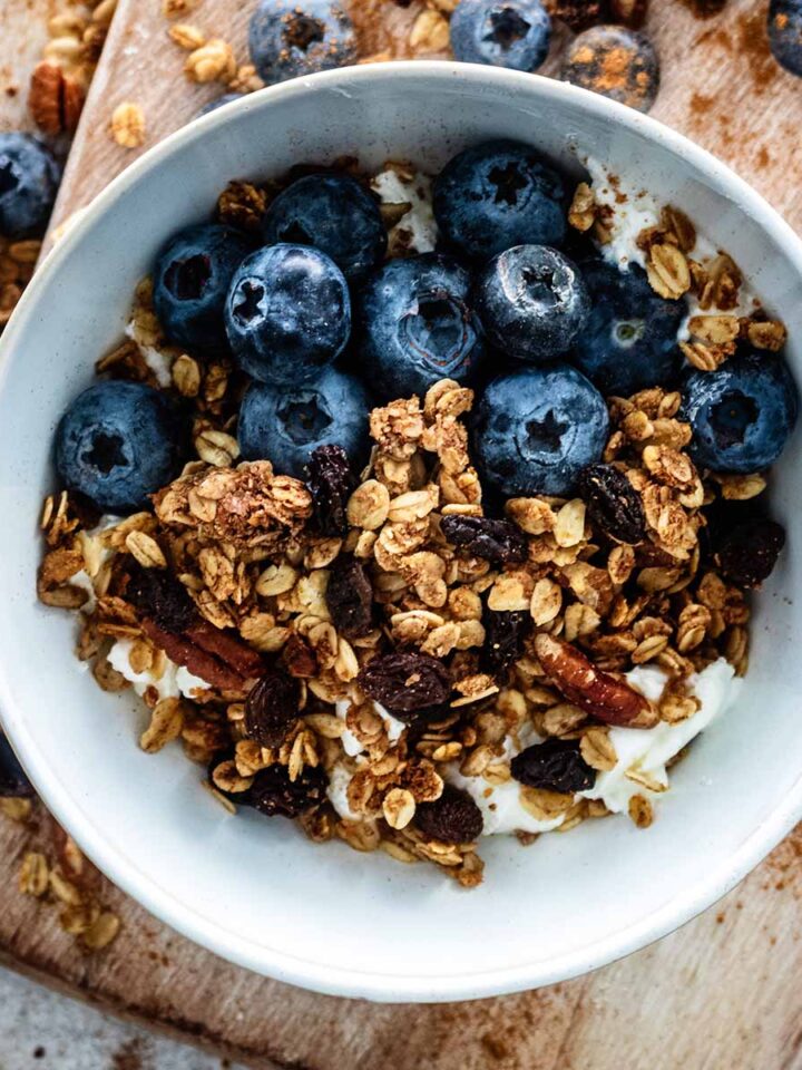 Cinnamon granola in a small white ceramic bowl with fresh blueberries.