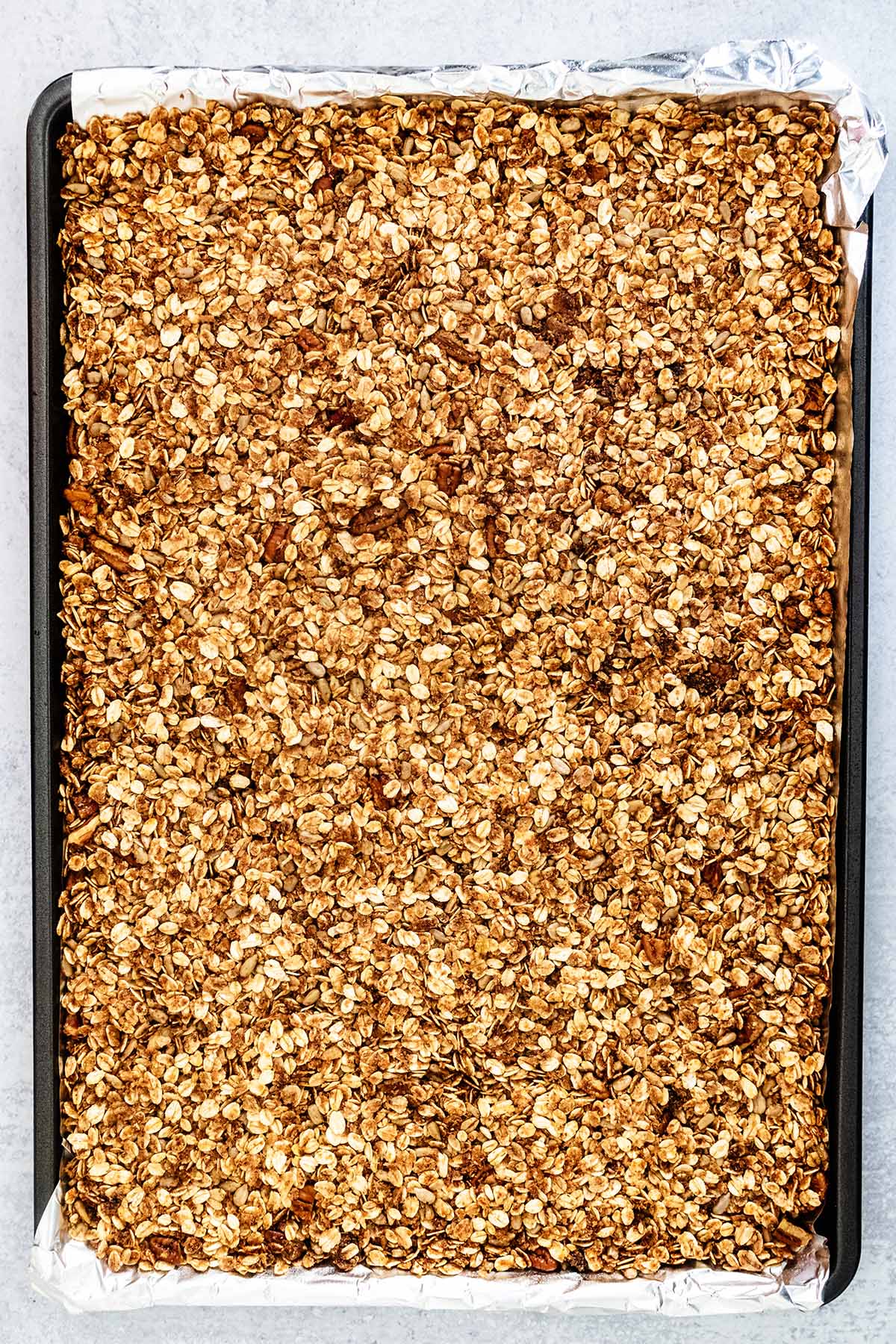 Unbaked cinnamon granola spread onto a foil-lined baking sheet.