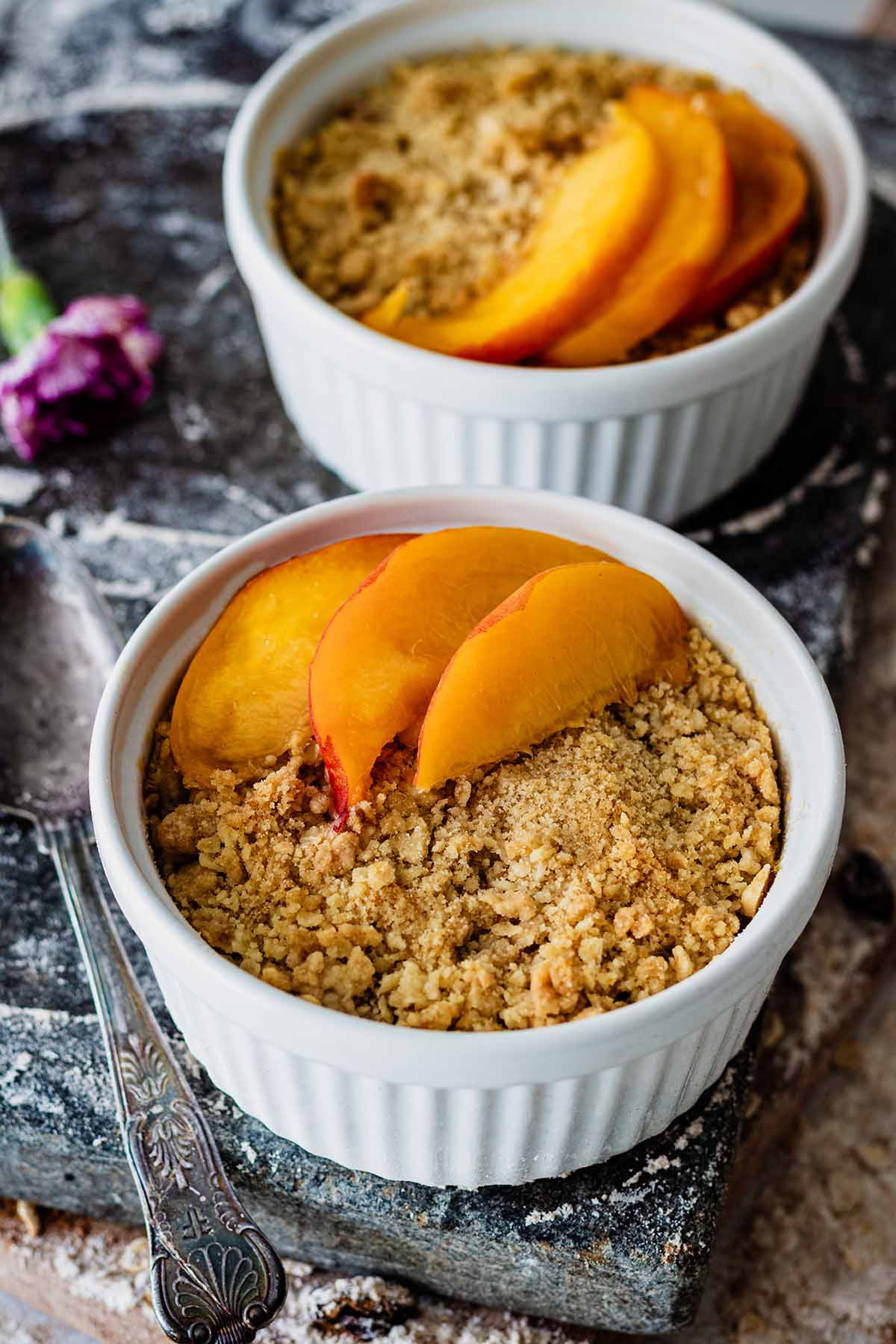 Fresh peach crumble topped with fresh peach slices in two white ramekins
