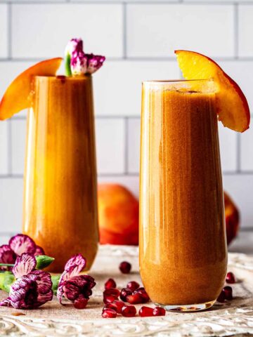 Two glasses of peach juice topped with peach slices and fresh flowers.