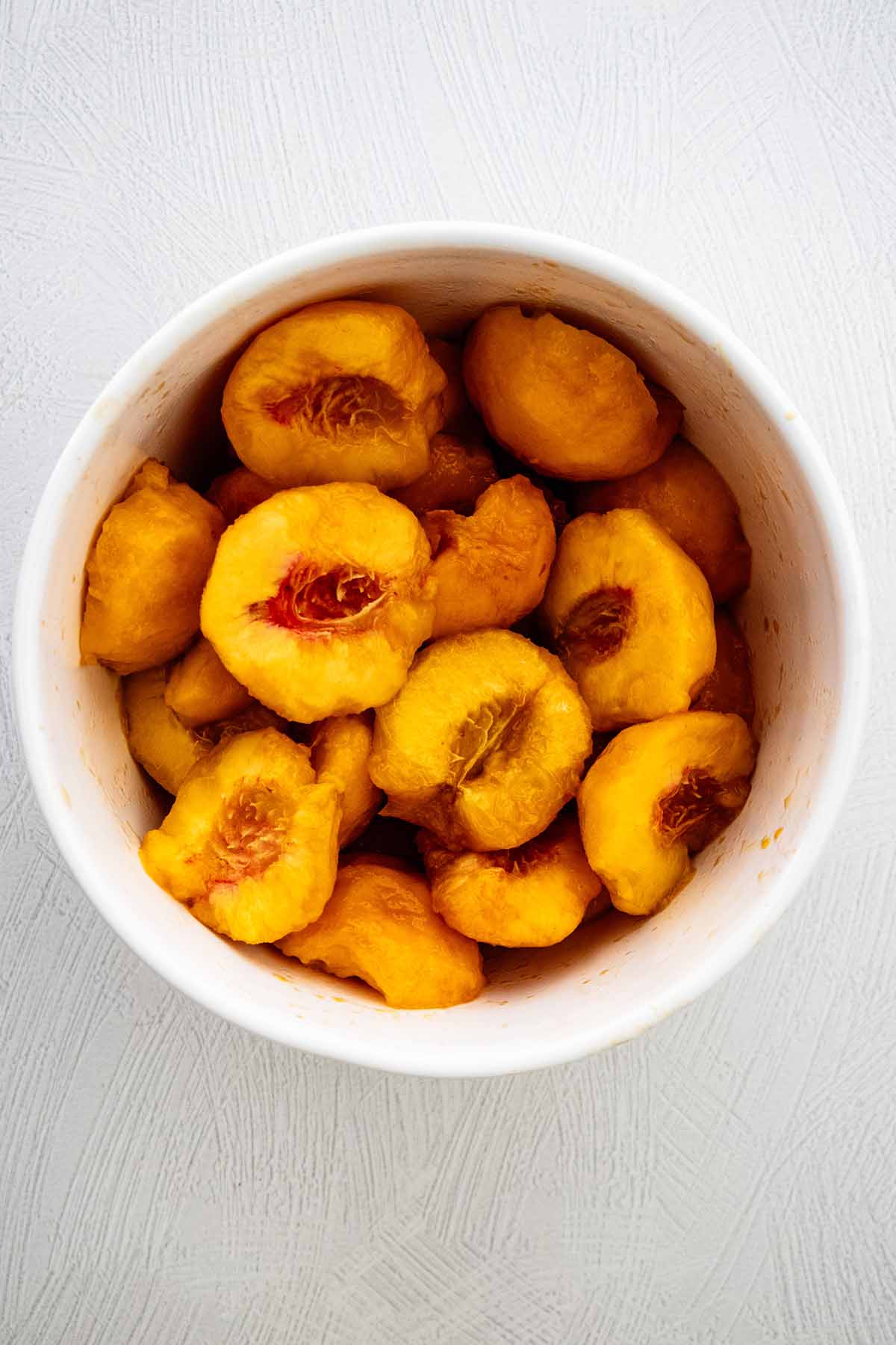 Peeled, pitted, and rough chopped peaches in a white ceramic bowl.