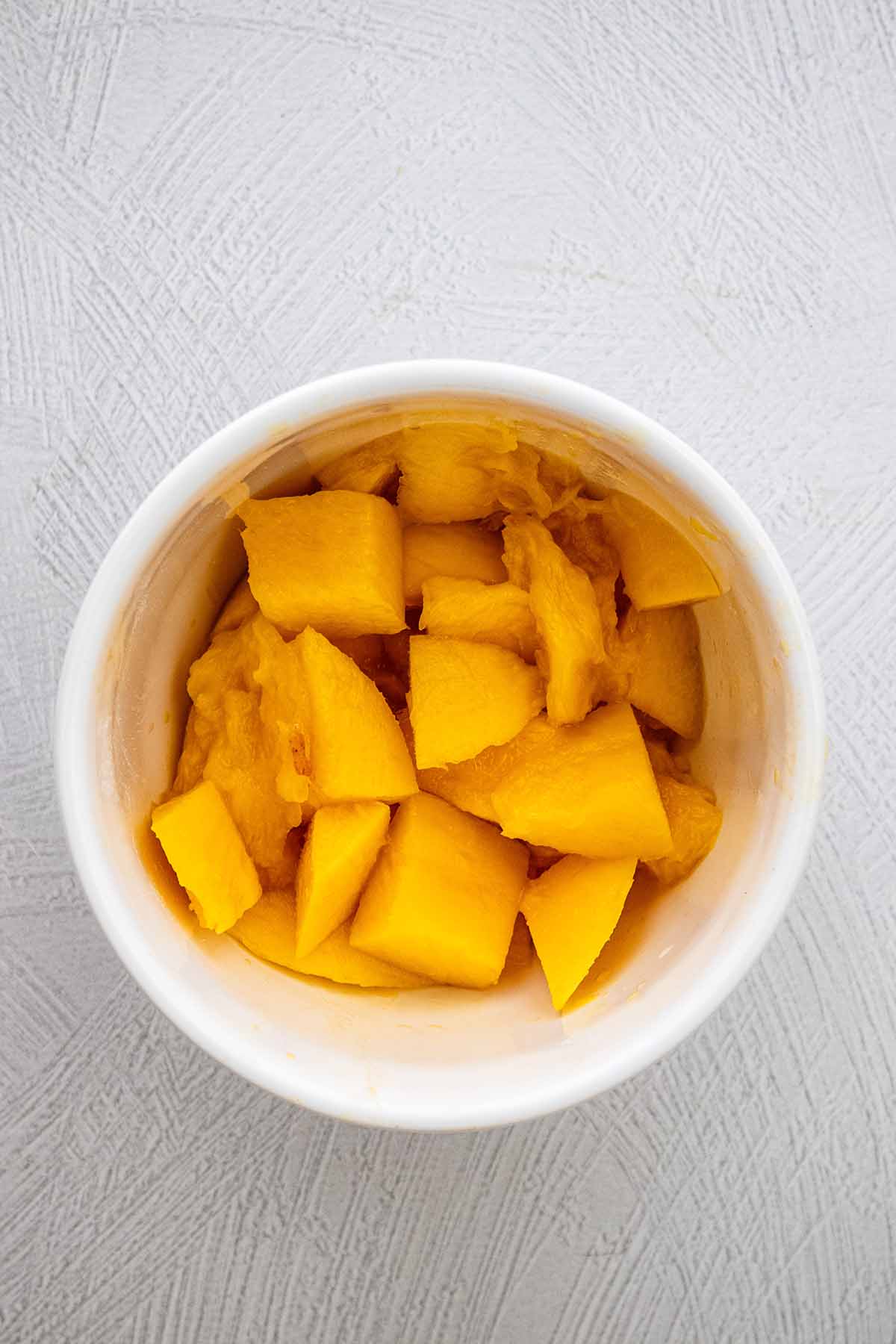Peeled, pitted, and chopped mango in a white ceramic bowl