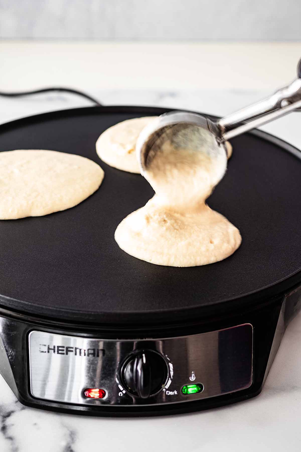 Pancake batter being ladled onto a griddle with an ice cream scoop.