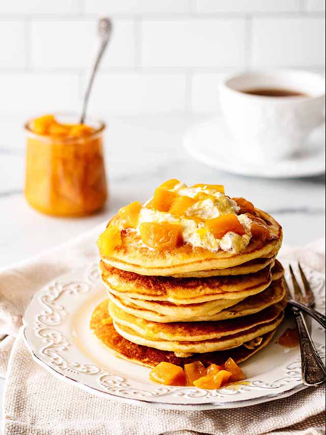 Stack of mango pancakes topped with mango compote on a white plate