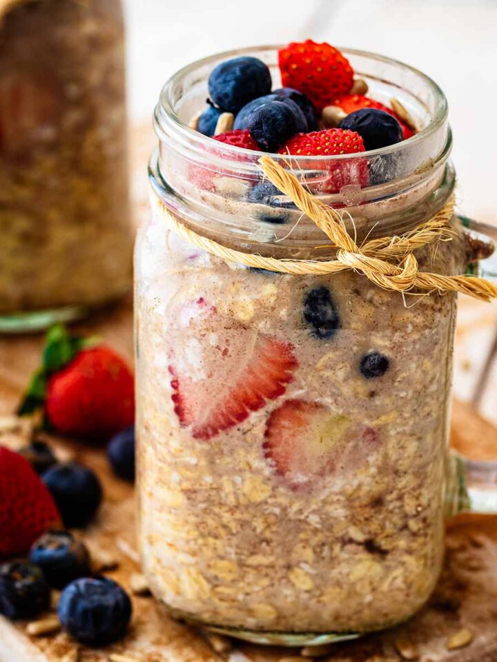 Close up of overnight oats without milk topped with sliced strawberries and fresh blueberries in a glass mug jar.