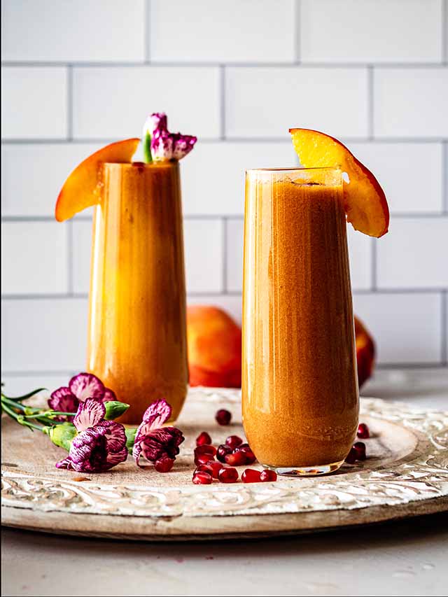 Two tall glasses of homemade peach juice topped with peach slices