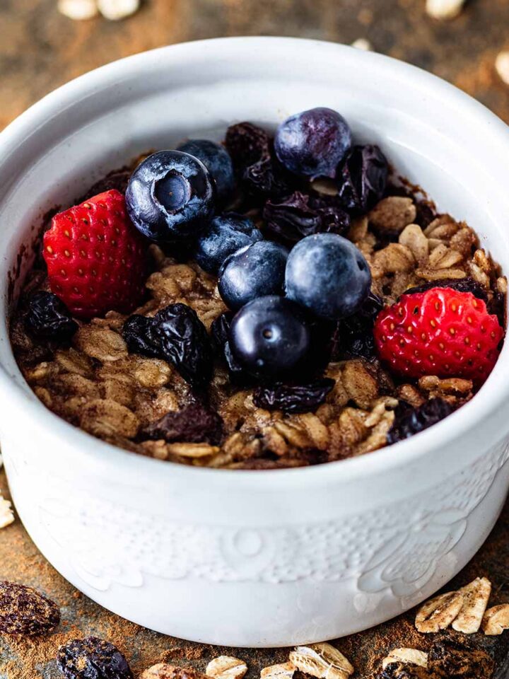 Single serving baked oatmeal topped with sliced strawberries and fresh blueberries in a white ceramic ramekin.