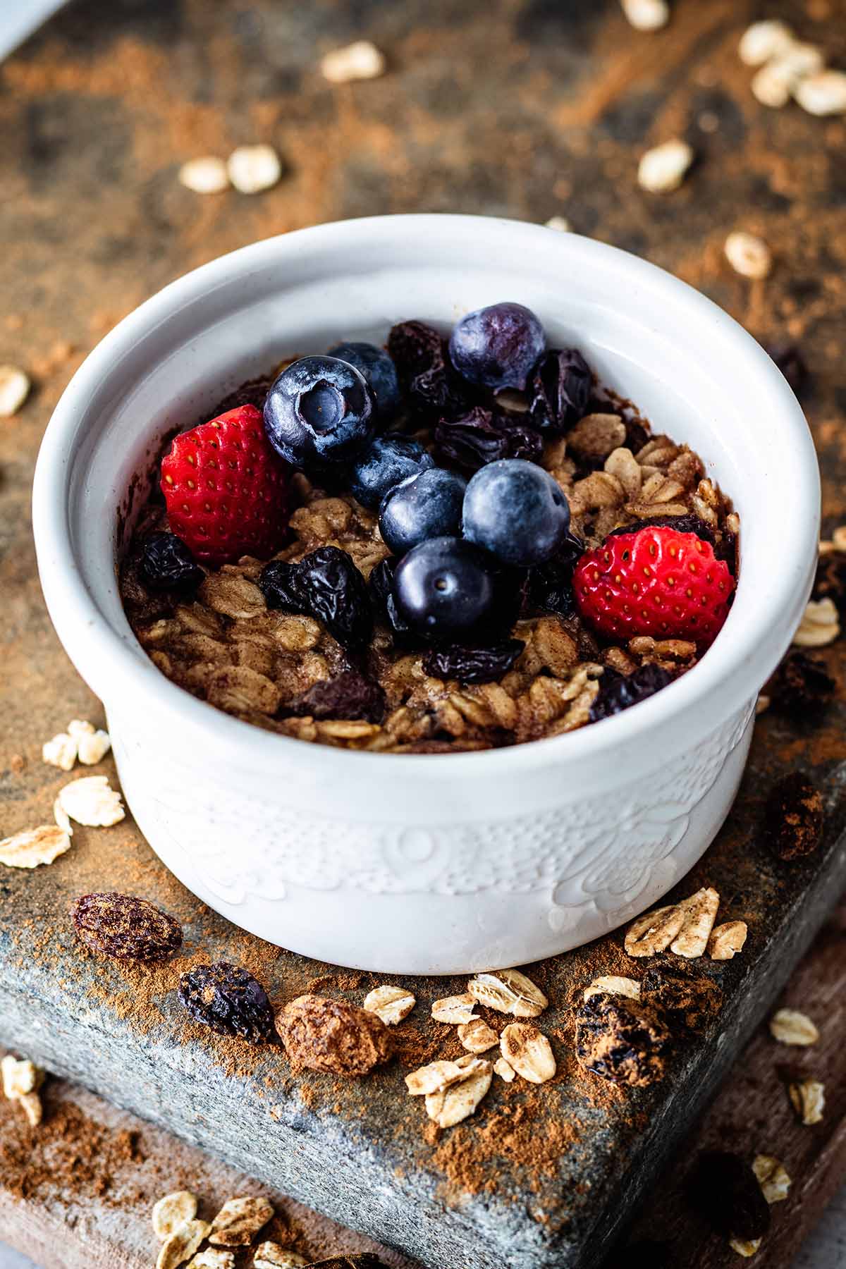 Single serving baked oatmeal topped with sliced ​​strawberries and fresh blueberries in a white ceramic ramekin.