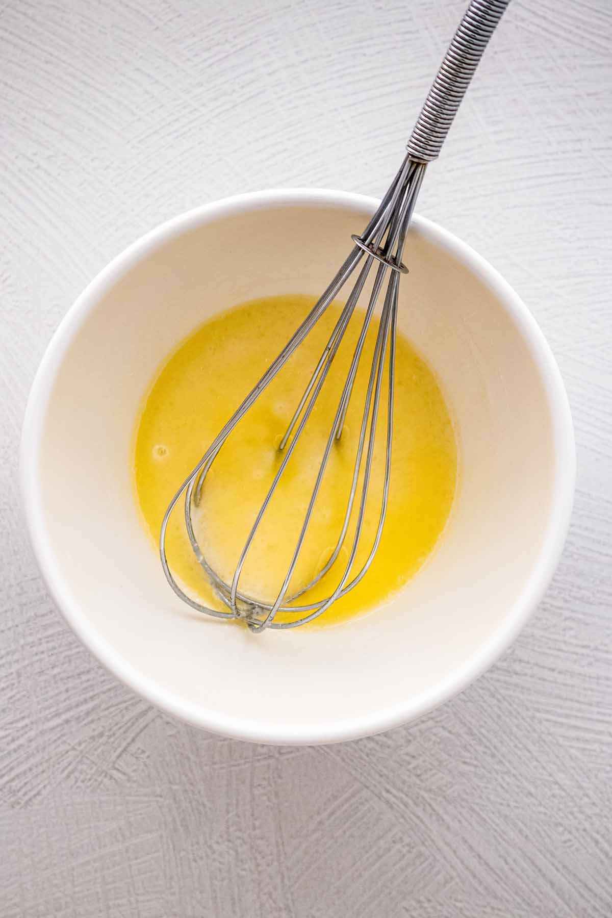 Wet ingredients in a white ceramic bowl with a whisk.