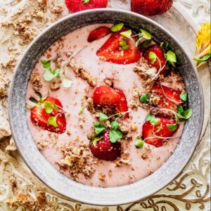 Strawberry banana smoothie bowl topped with sliced ​​strawberries and micro greens in a gray bowl.