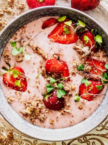 Strawberry banana smoothie bowl topped with sliced strawberries and micro greens in a grey bowl.