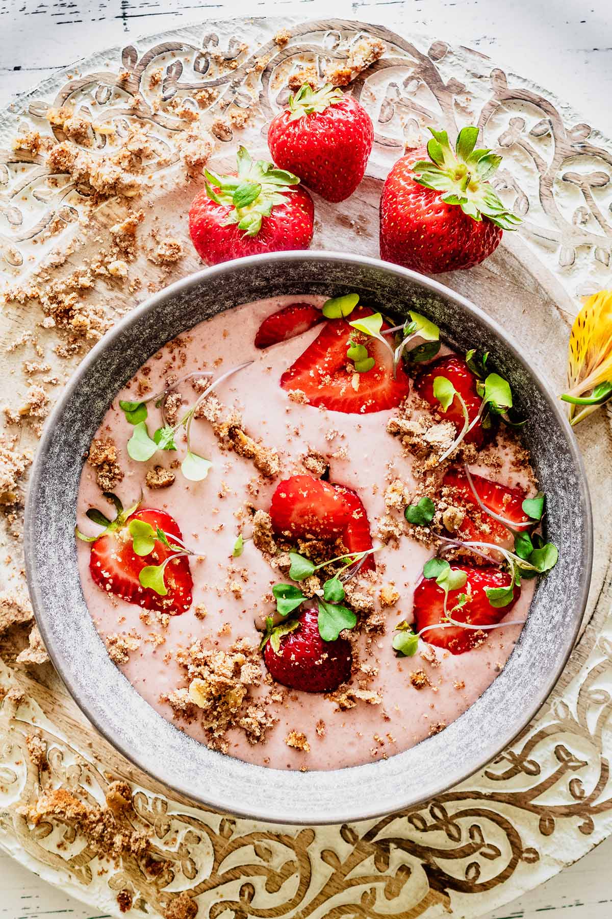 Strawberry banana smoothie bowl topped with sliced strawberries and micro greens in a grey bowl.