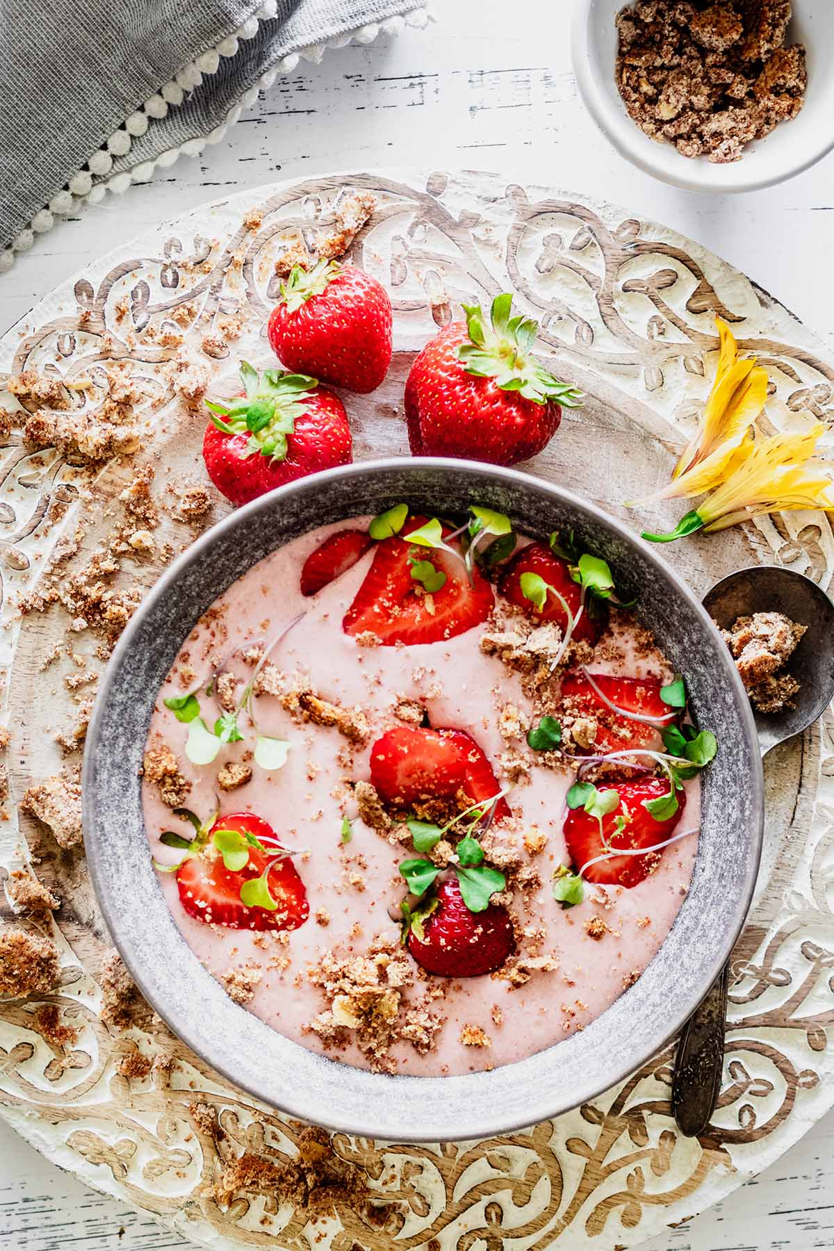 Strawberry banana smoothie bowl topped with sliced ​​strawberries, crumble, and micro greens in a gray bowl with fresh whole strawberries off to the side.