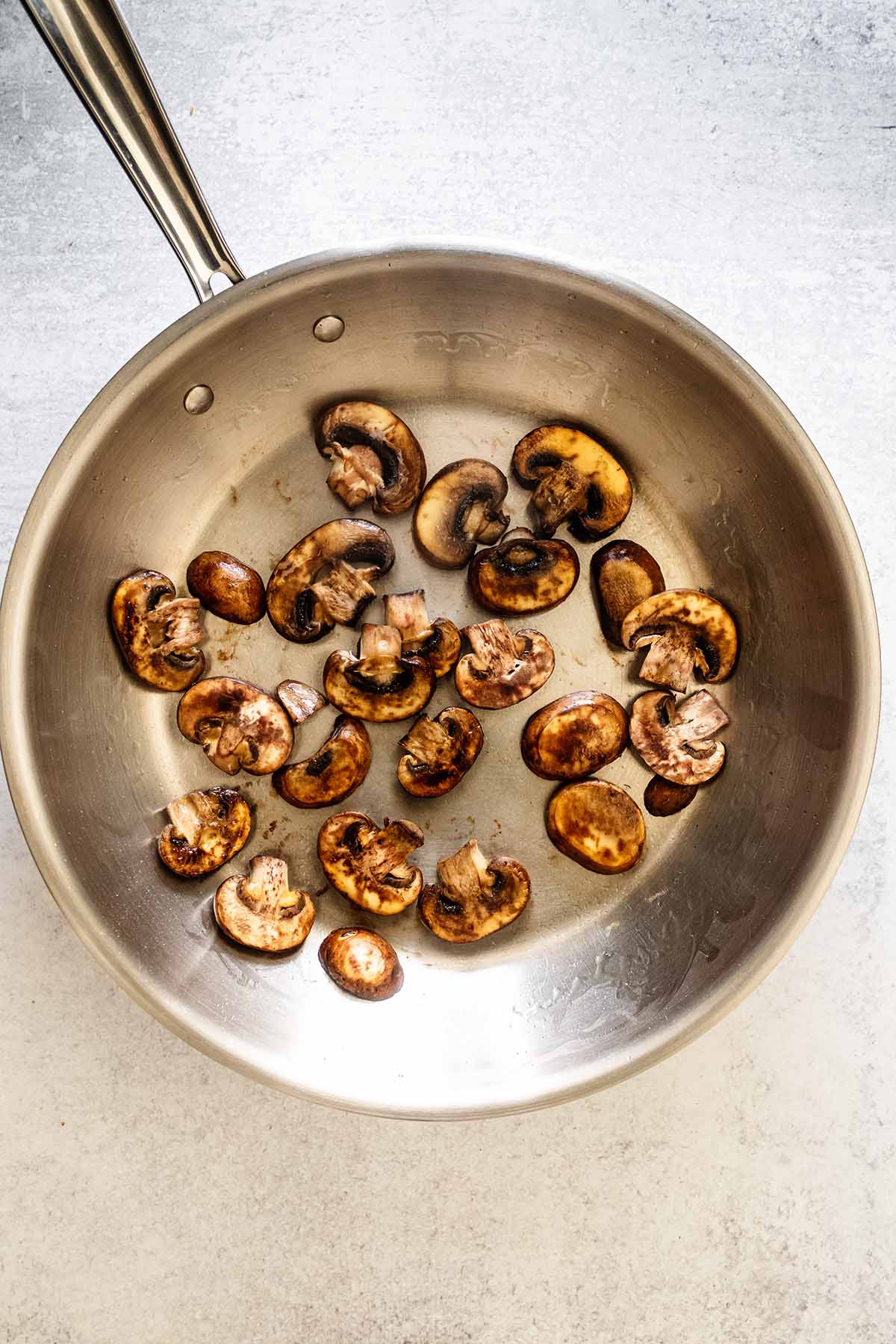 Cooked sliced ​​mushrooms in a stainless steel skillet.