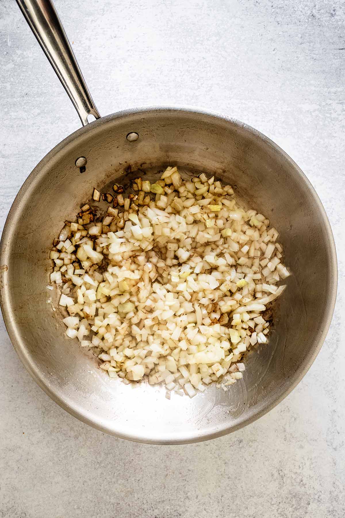 Cooked diced onion in a stainless steel skillet.