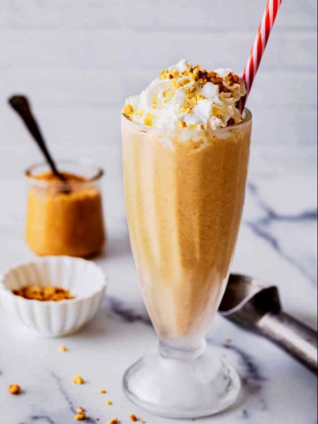 Peanut butter milkshake in a tall shake glass topped with whipped cream and chopped peanuts and a red and white straw