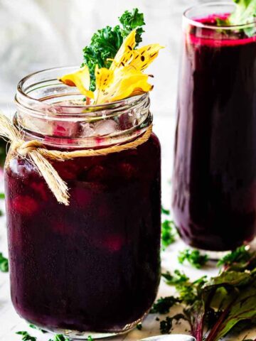 A glass mug and tall glass filled with beet green juice garnished with kale.