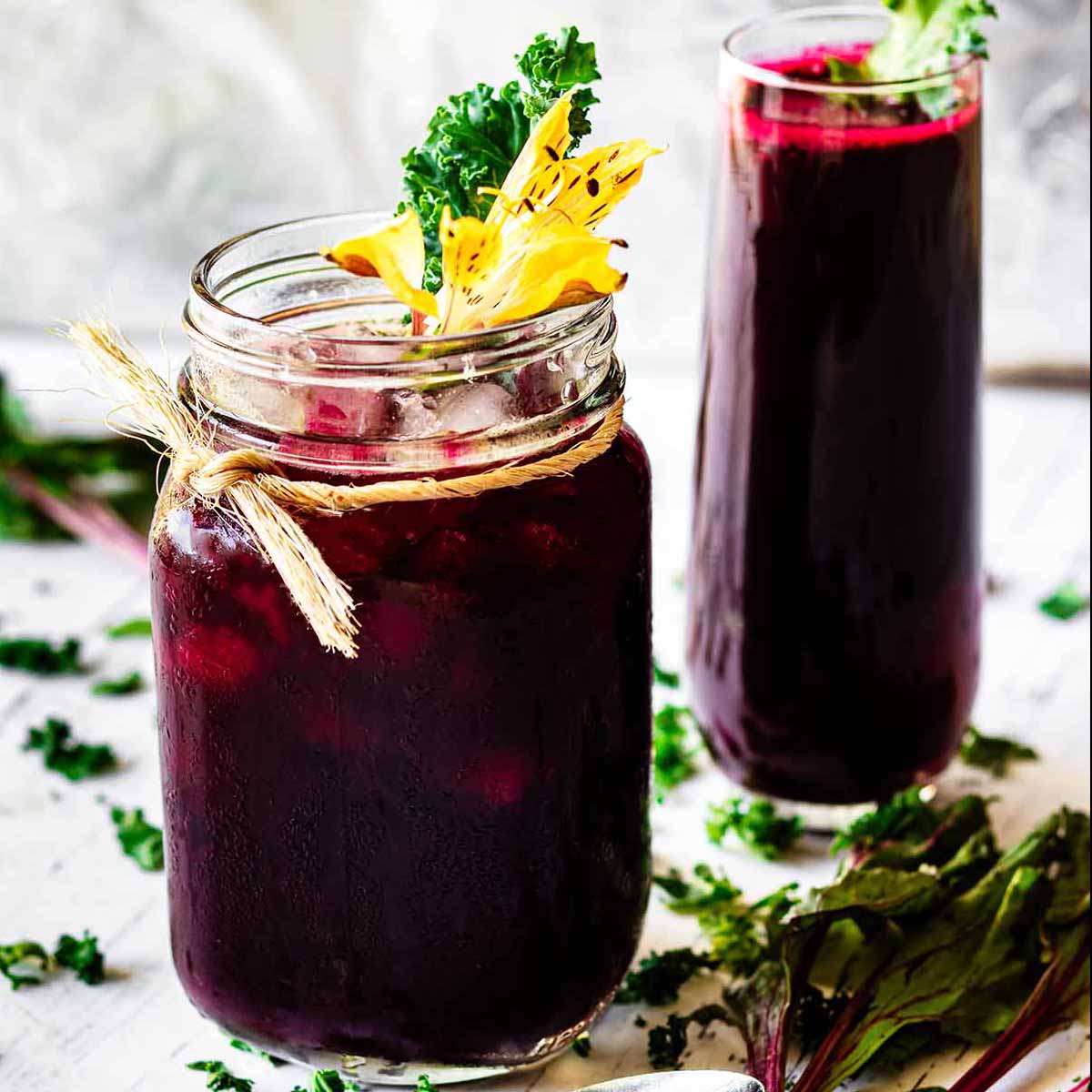 A glass mug and tall glass filled with beet green juice garnished with kale.