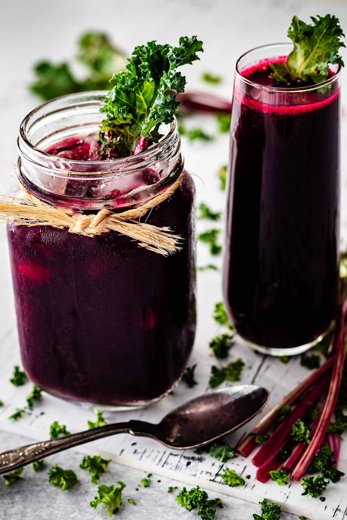 Close up of glass mug and tall glass filled with beet green juice garnished with kale.