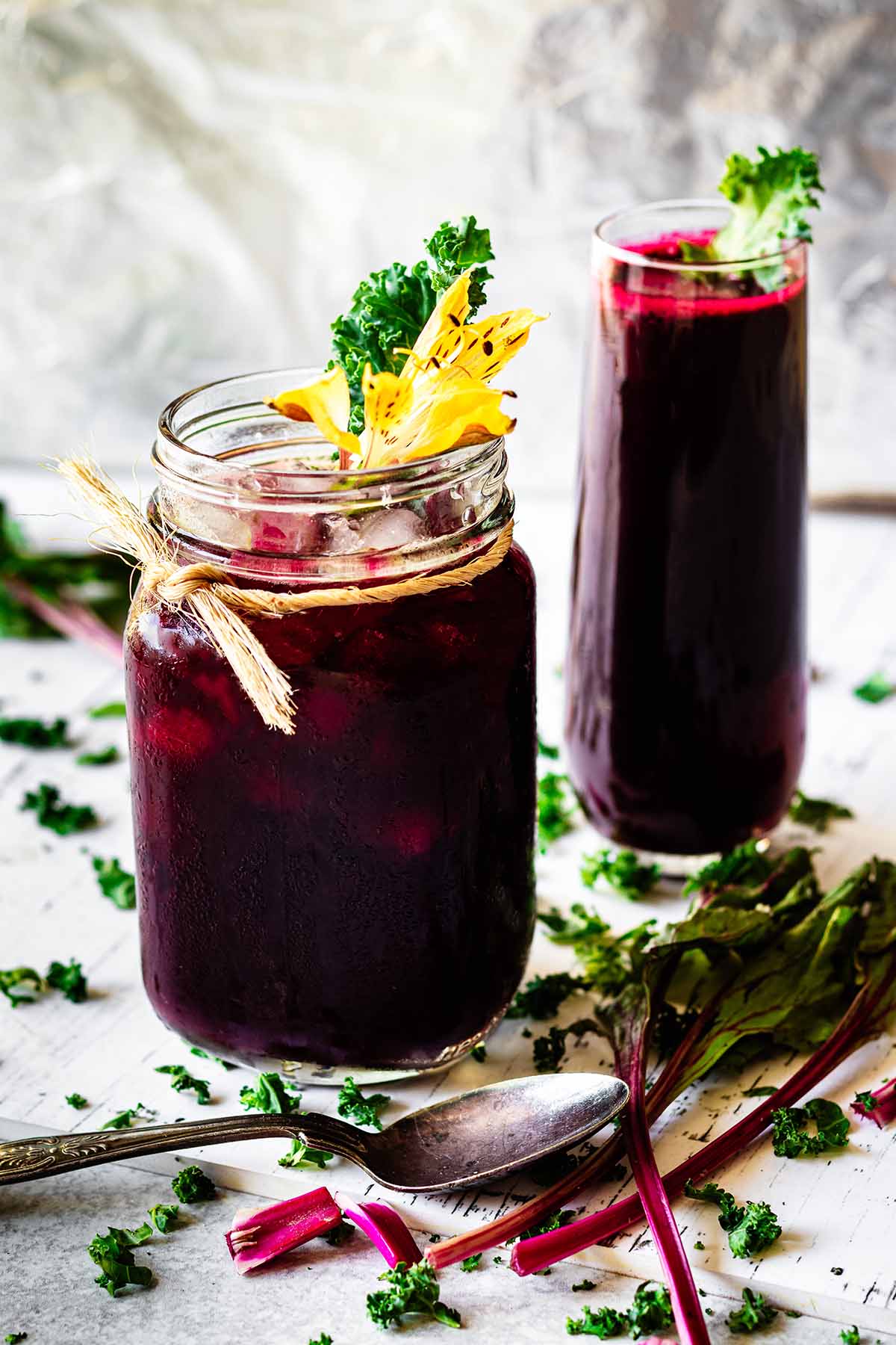 A glass mug and tall glass filled with beet green juice garnished with kale.