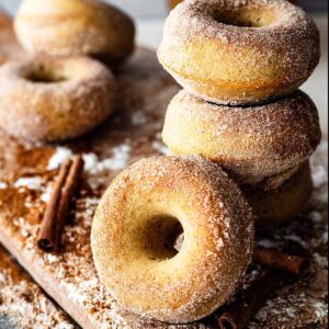 Gluten free apple cider donuts stacked on a wooden cutting board.