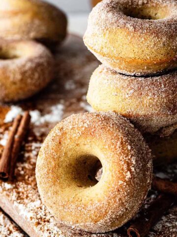 Gluten free apple cider donuts stacked on a wooden cutting board.