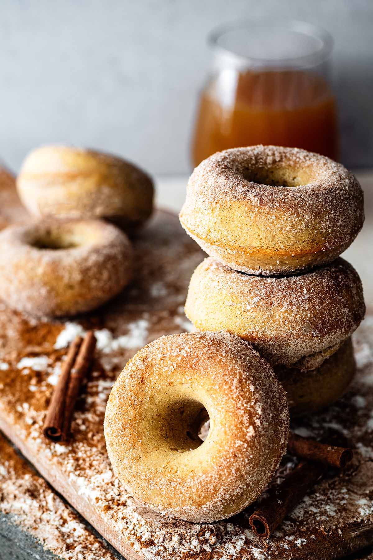 Gluten free apple cider donuts stacked on a wooden cutting board.
