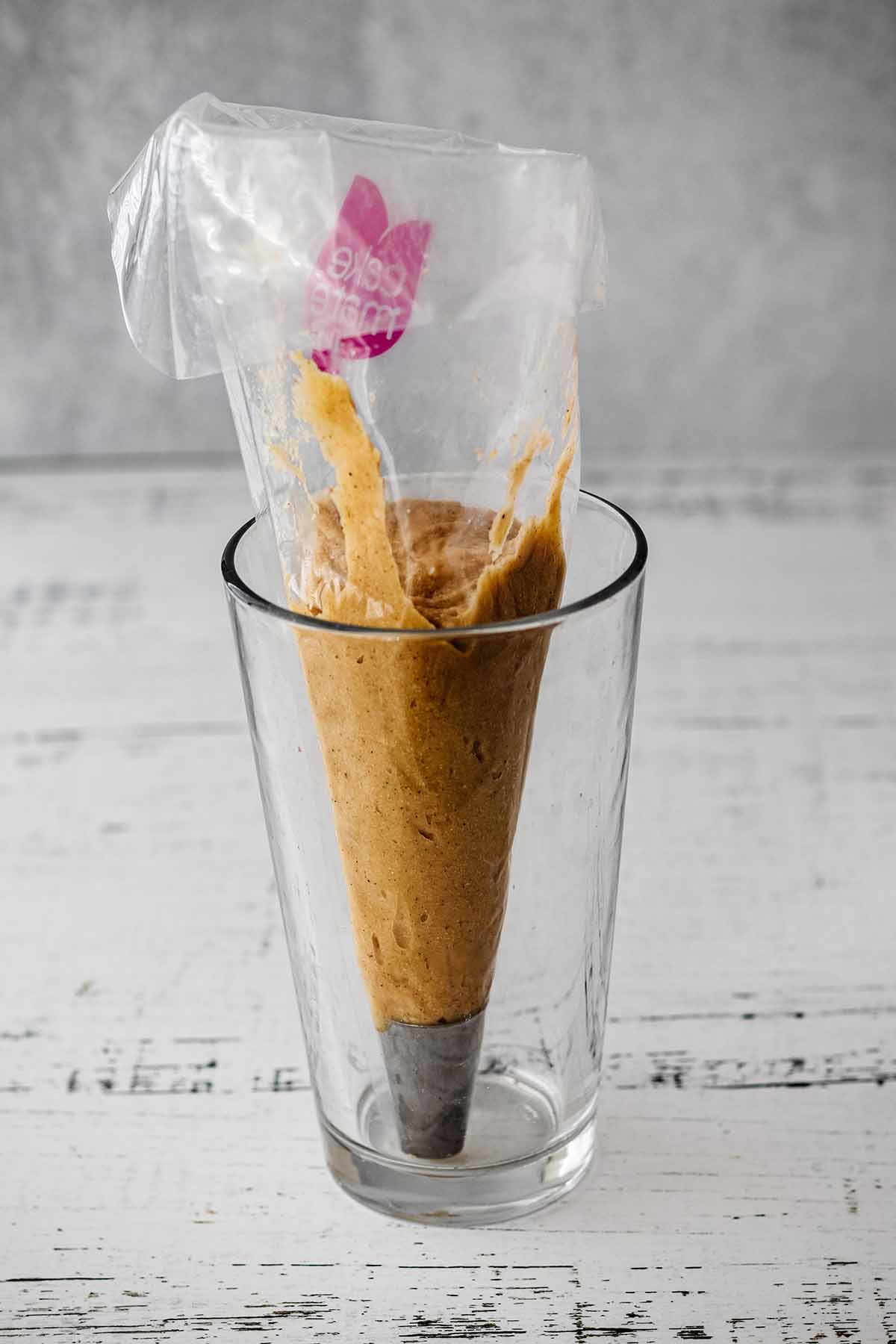 Apple cider donut batter in a disposable piping bag in a tall glass.