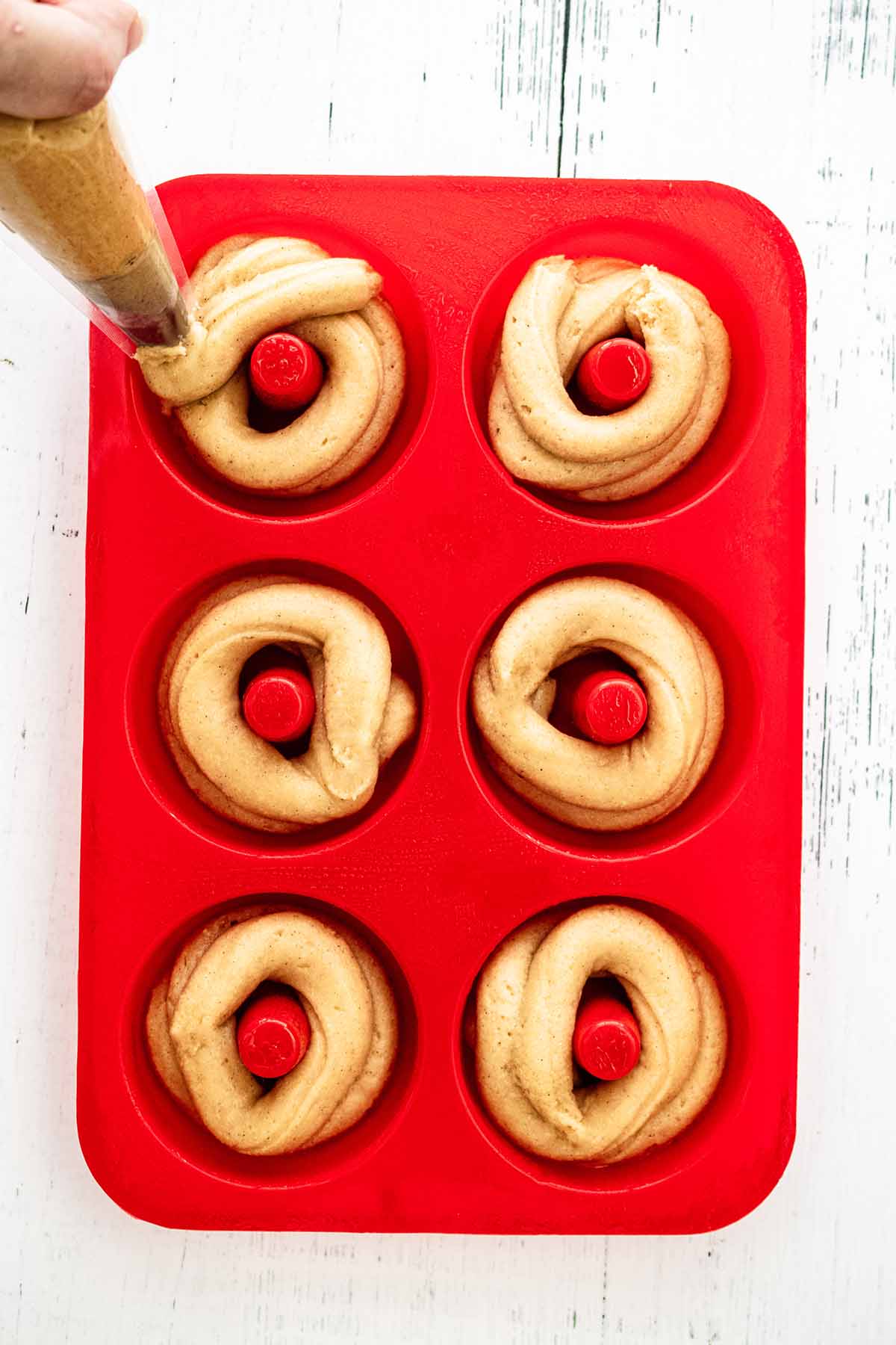 Donut batter being piped into a red silicone donut pan.