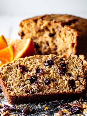 Close up of a slice of sweet breakfast bread with sliced oranges and a sweet bread loaf.