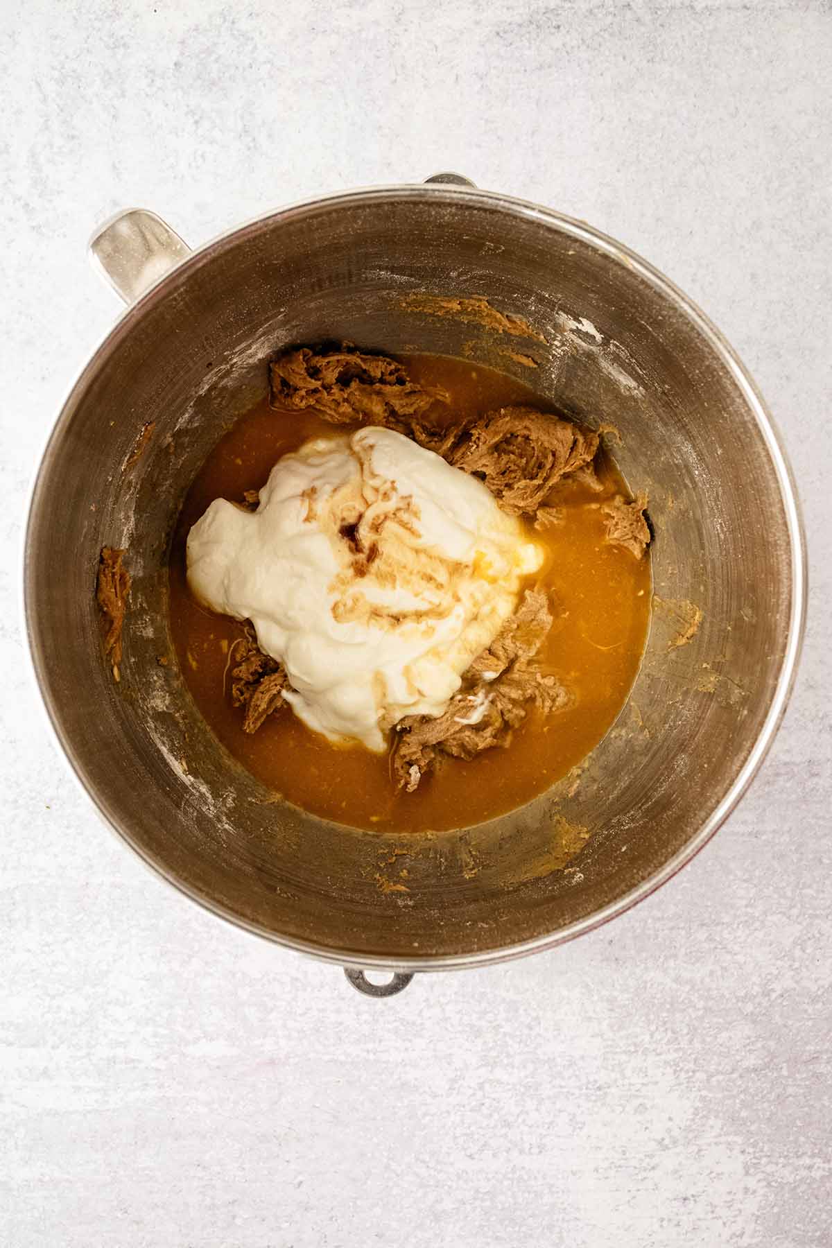 Yogurt, vanilla, and orange juice with batter in a large metal mixing bowl.