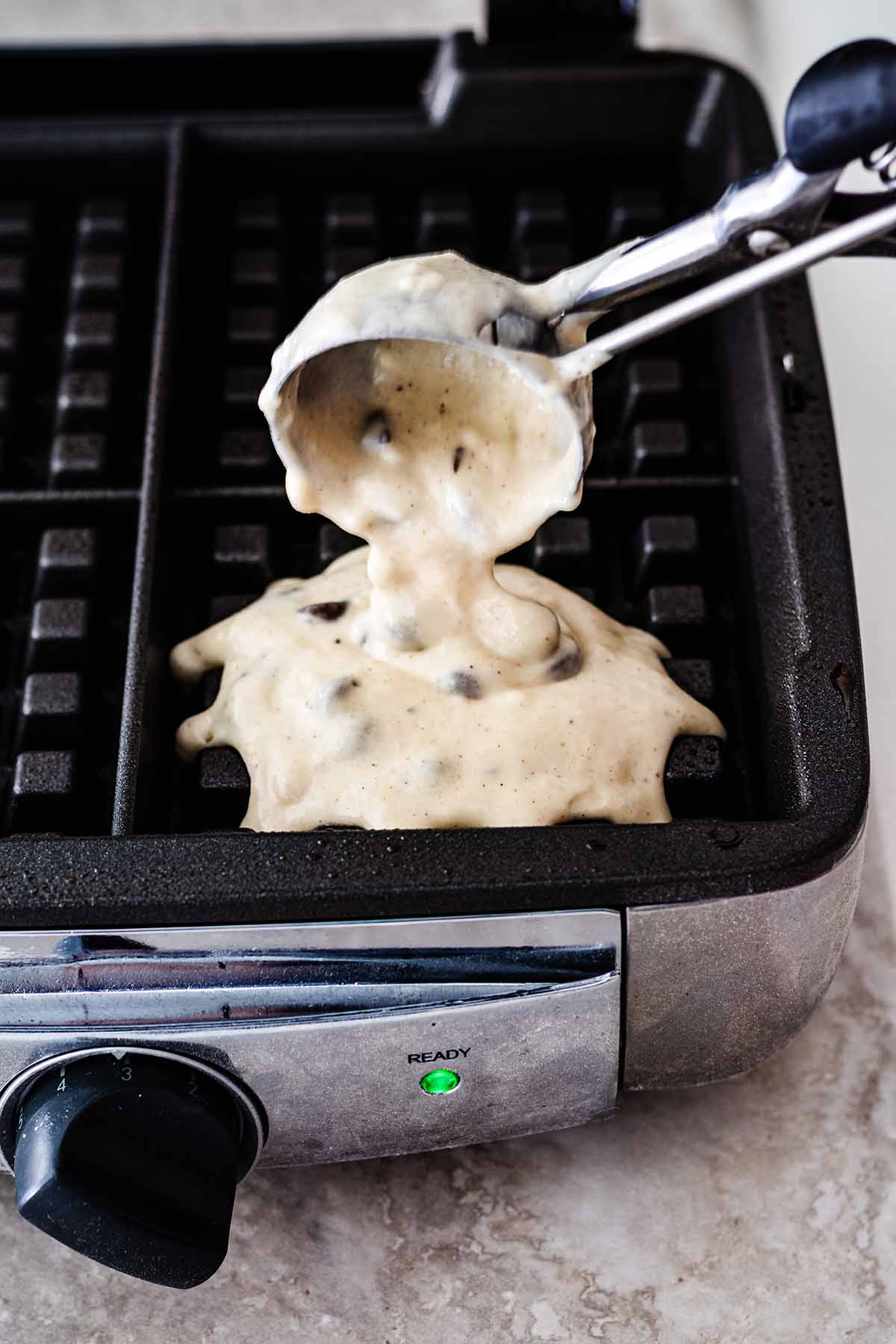 Waffle batter being scooped onto waffle iron.